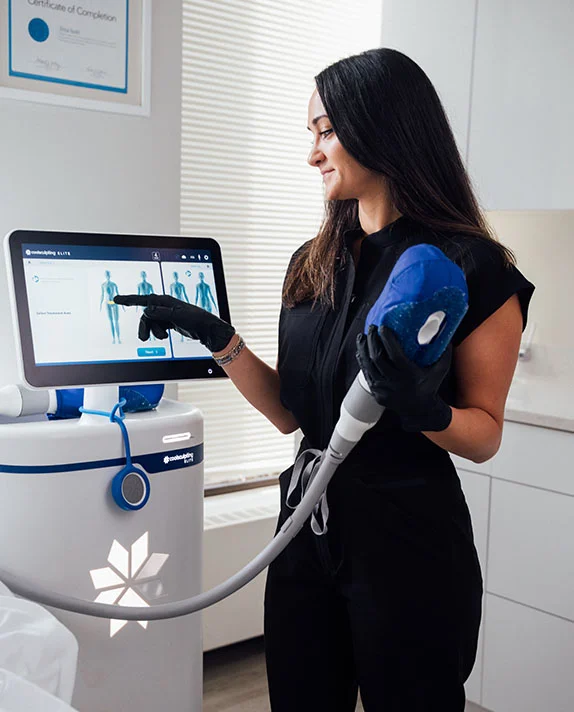 A medical professional at Dr. Pathak's practice demonstrating the CoolSculpting Elite system to a patient resting comfortably in a treatment room.
