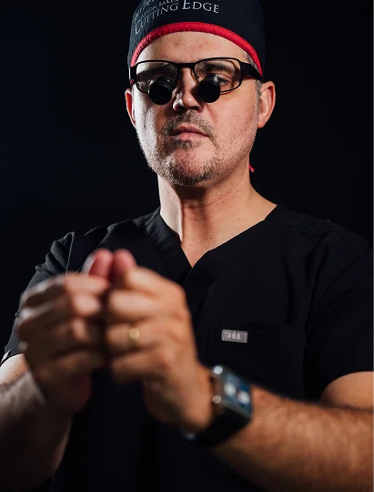 A close-up, high-detail shot of Dr. Abraham Pathak wearing black surgical scrubs and specialized surgical loupes (magnifying glasses), emphasizing precision and focus.