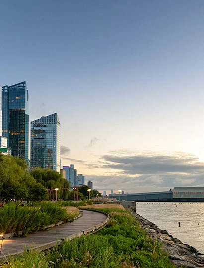 A scenic view of a waterfront boardwalk with city skyscrapers in the background during twilight.